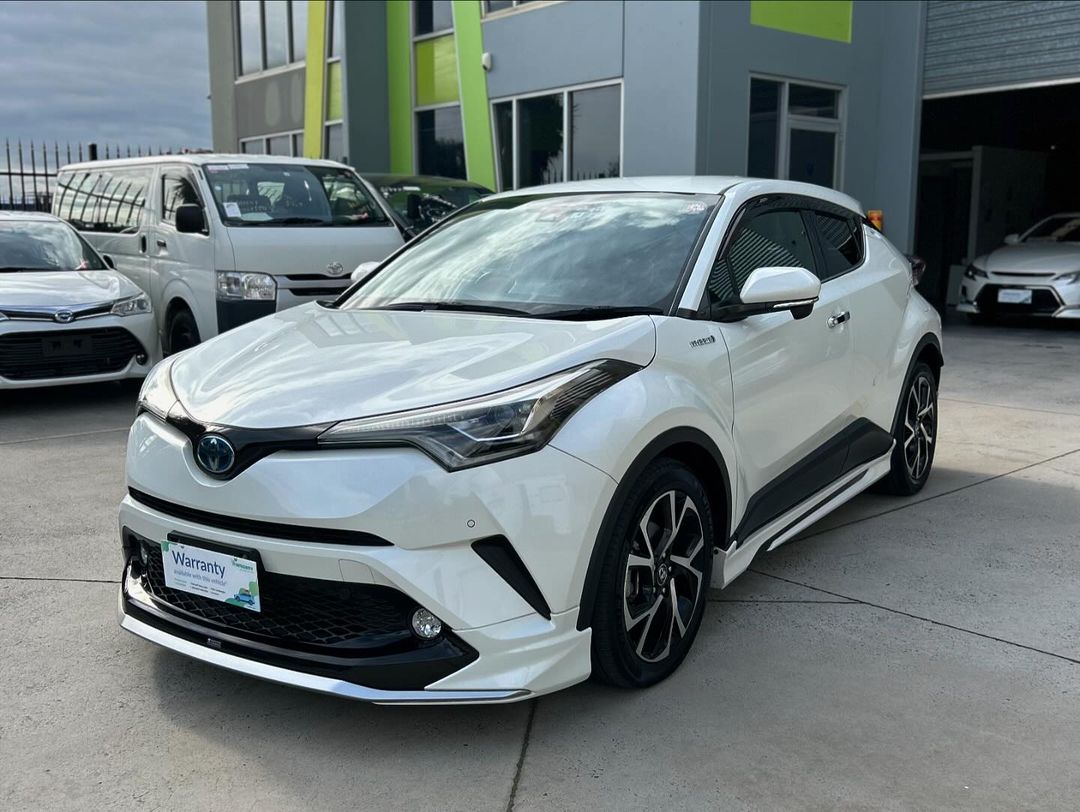 White Toyota C-HR parked in front of a building on a sunny day.