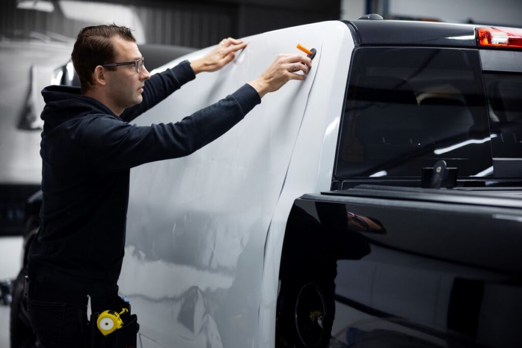 A man painting the side of a truck with a brush, adding color and detail to the vehicle's surface.