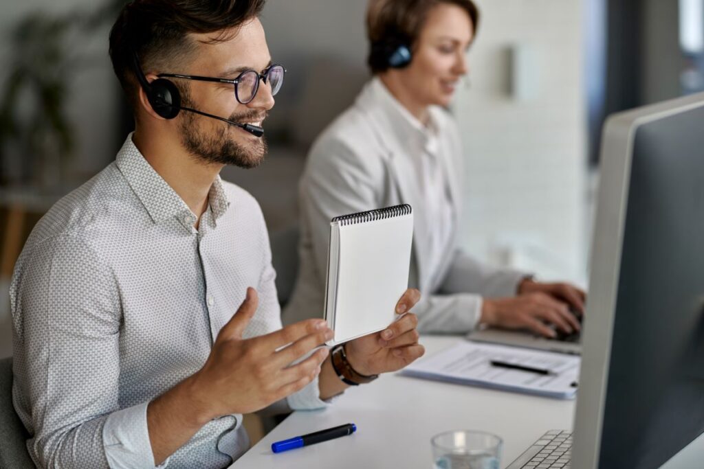 A man and woman wearing headsets, collaborating on a computer.