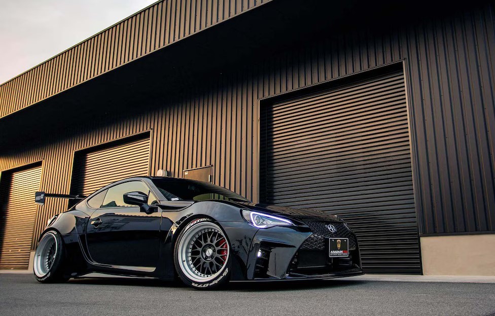 Black sports car parked in front of garage, sleek design and shiny finish, ready for a drive.